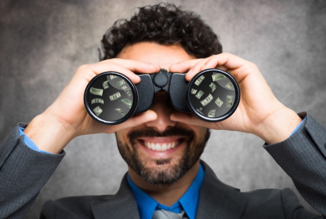 Businessman using binoculars, money reflected in the lens