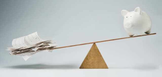 Piggy bank balancing on seesaw over a stack of bills