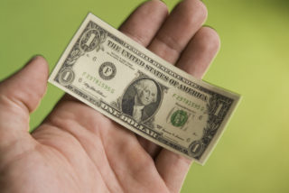 a hand holding a miniature United States one dollar bill depicting the shrinking United States dollar